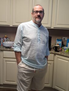 A man in a light blue shirt. He has close cropped brown hair and a salt and pepper beard.
